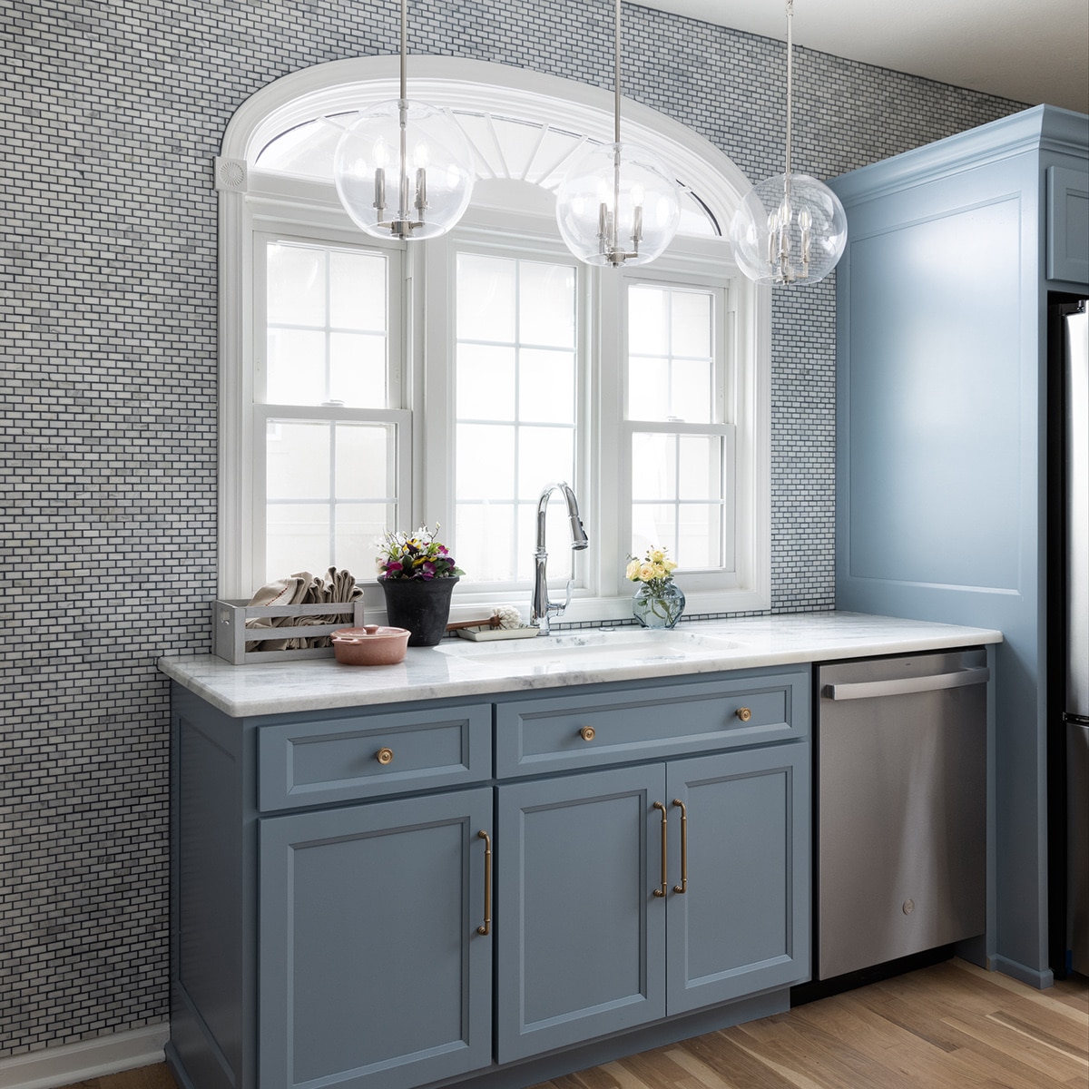 Kitchen pantry with light blue cabinets, silver sink and dishwasher, white marble slab countertop, and a white marble look brick joint mosaic on the walls and backsplash.