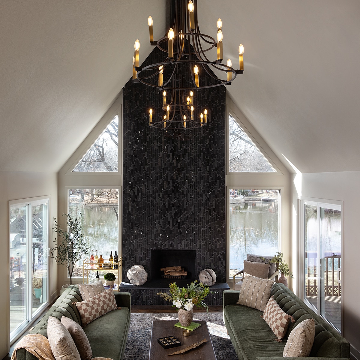 Living room with white walls, green couches, and a fireplace with floor to ceiling black mosaic tile and black granite on the hearth.