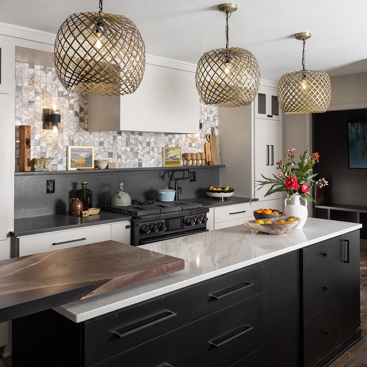 Kitchen with white cabinets, island with black cabinets and a beige marble countertop, range with black countertop and backsplash, and the top half of the wall using natural stone mosaic.
