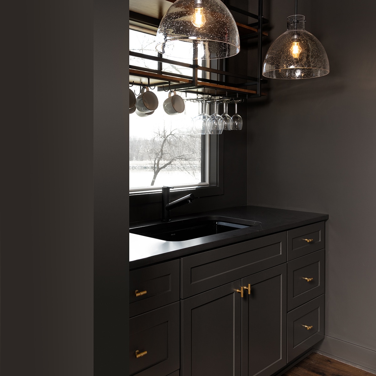 Wet bar with dark walls and cabinets with a black countertop.