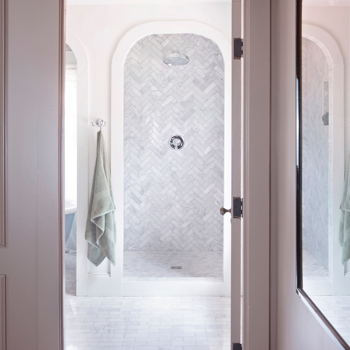 Shower with white natural stone herringbone mosaic on the walls while a matching hexagon mosaic graces the shower floor, and white marble look brick joint tile on the bathroom floor.