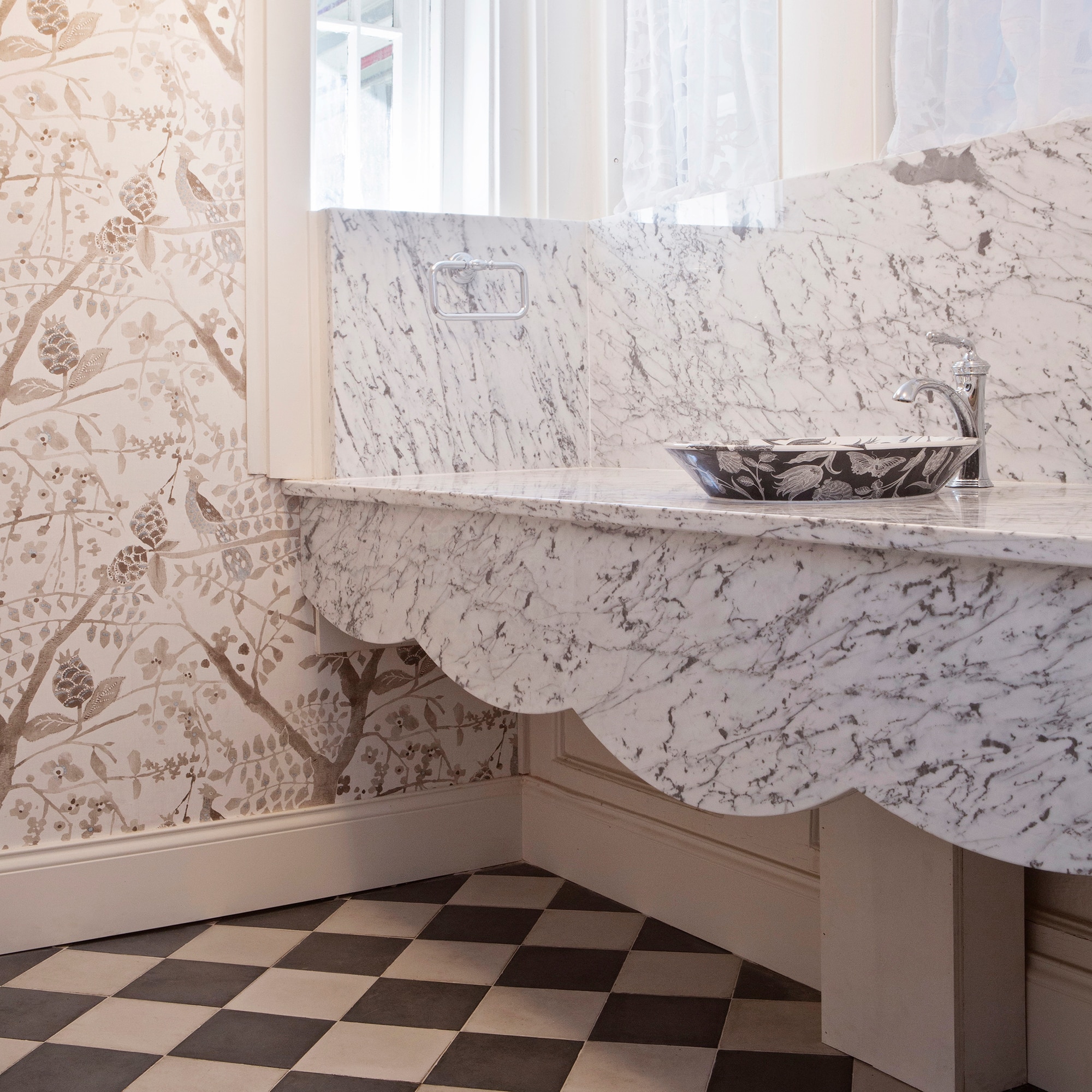 Half bath with gray and cream checkered floor tile, white marble slab on the countertop and backsplash, and floral wallpaper.
