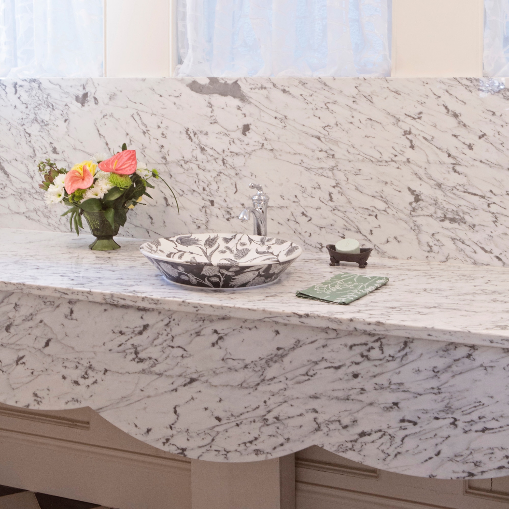Bathroom sink with white marble slab on the countertop and backsplash, and a decorative floral vase.