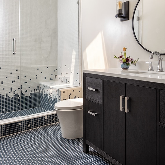 Bathroom with a dark wood vanity, white quartz countertop, and square mosaic tile in blue and white on the shower walls and floor.