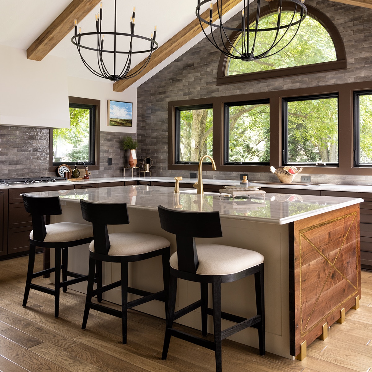 Kitchen with center island, white sitting stools, brown cabinets, light wood floors, white quartzite slab countertop, and gray undulated subway tiles on the walls.