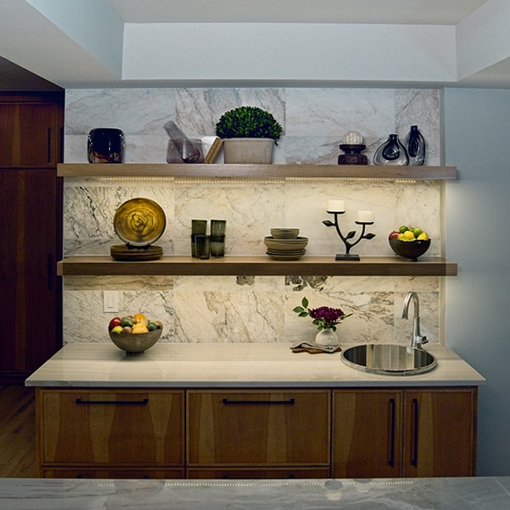 Breakfast bar with a white marble look tile on the wall, a white quartzite countertop, and wood cabinets.