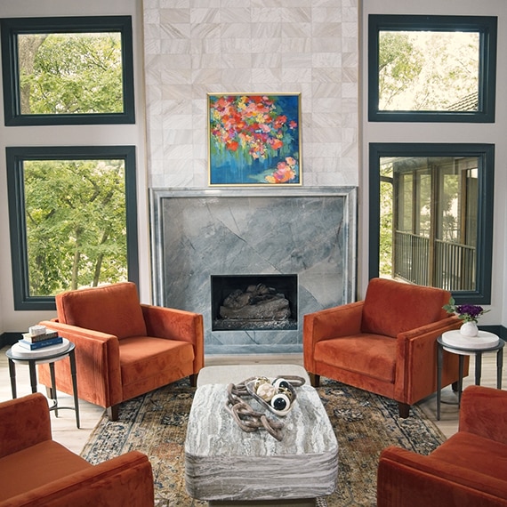 Living room with orange sitting chairs, light wood floors, gray quartzite wrapped around the fireplace, and a white marble look mosaic going up the wall above the fireplace.