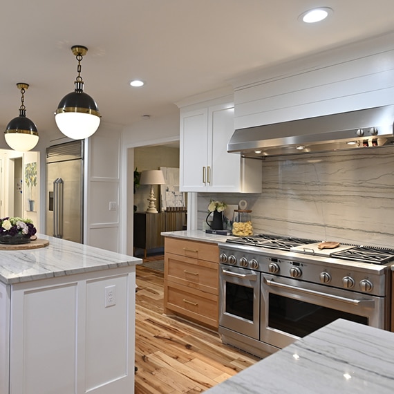 Remodeled kitchen with gray heavily veined quartzite countertop, backsplash, and island, natural wood cabinets, and industrial-sized stainless steel gas stove/oven.