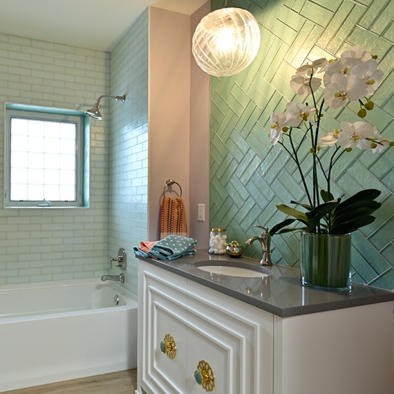 Small bathroom with light green glass tile backsplash, vanity with gray quartz counter and silver faucet, and mint glass subway shower tile.