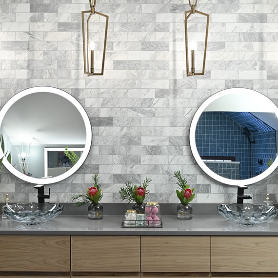 Renovated bathroom vanity with 2 glass vessel sinks, black faucets, gray marble tile backsplash, gray quartz countertop, and wall-mounted round lighted mirrors.