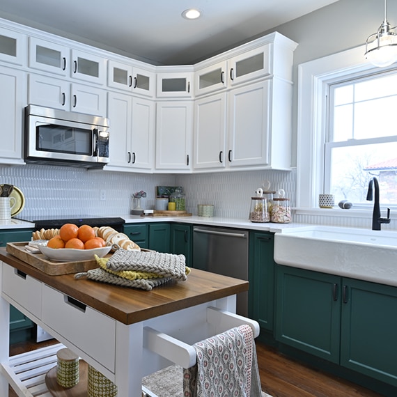 Farm house kitchen with white picket tile backsplash, white quartz countertops, large farm sink, butcher block island, dark green lower & white upper cabinets.