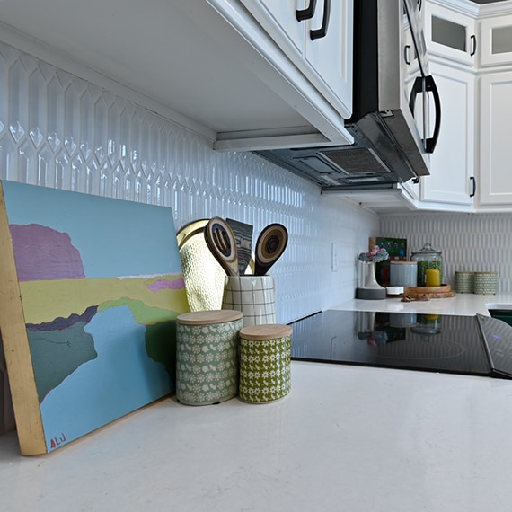 Closeup of farm house kitchen with white picket tile backsplash, white quartz countertops, and white upper cabinets.