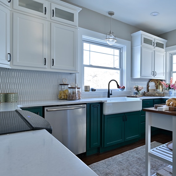 Farm house kitchen with white picket tile backsplash, white quartz countertops, large farm sink, butcher block island, dark green lower & white upper cabinets.