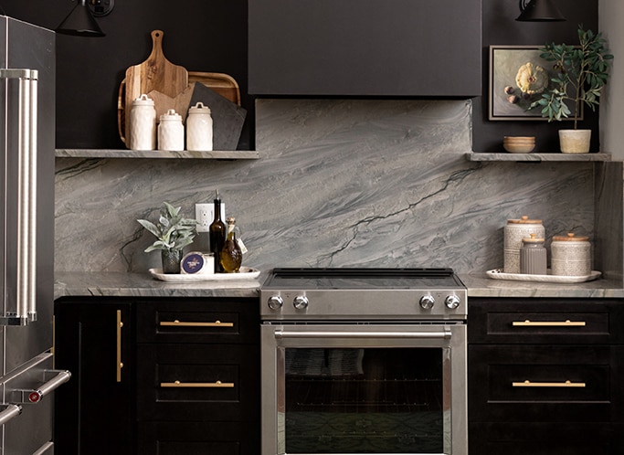 Kitchen with black cabinets, gray quartzite countertop and backsplash, and silver appliances.