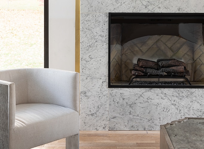 Fireplace with white marble look slab surrounding it, light wood floor, and a white sitting chair.