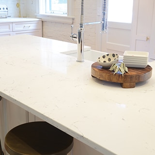 Closeup of kitchen island with white & gray veining quartz countertop and sink with polished silver faucet.