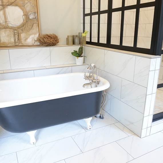 Renovated bathroom with white & gray tile that looks like marble on the floor and wainscot behind a free-standing claw-footed bathtub.