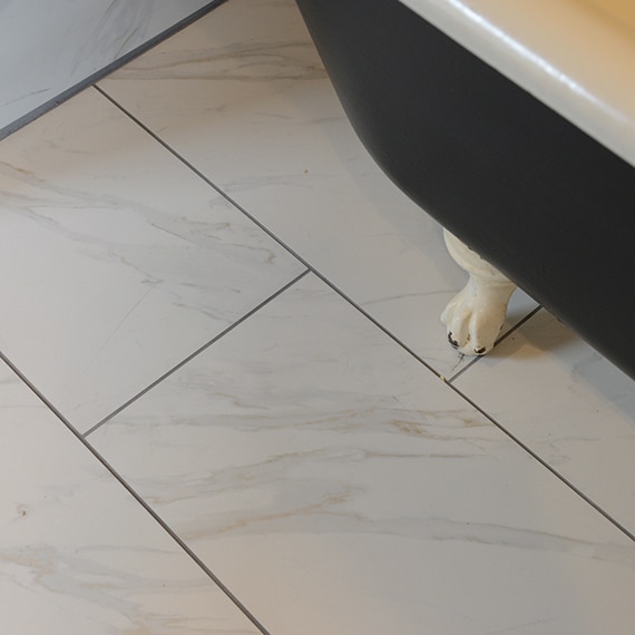 Closeup of white & gray tile that looks like marble on the floor under a free-standing claw-footed bathtub.