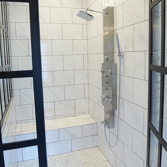 Renovated bathroom with white & gray tile that looks like marble on the walls, bench, and floor of a walk-in steam shower.