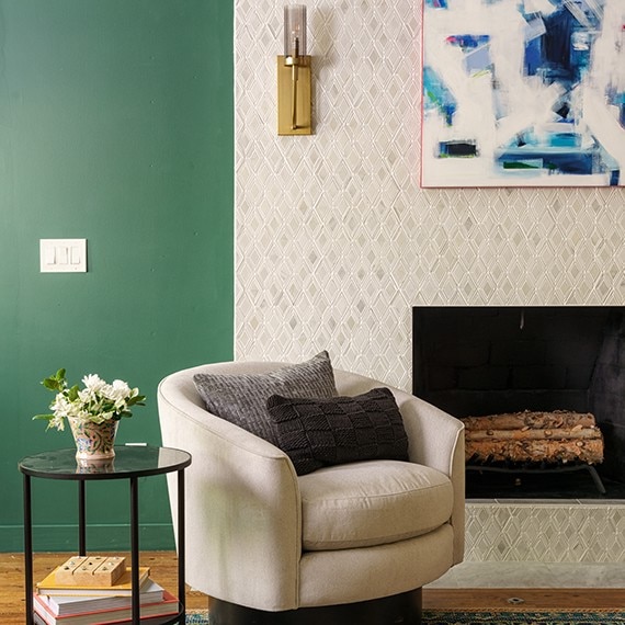 Renovated family room with green painted walls, fireplace façade of white & gray natural stone diamond mosaic tile, and white over-stuffed chair.