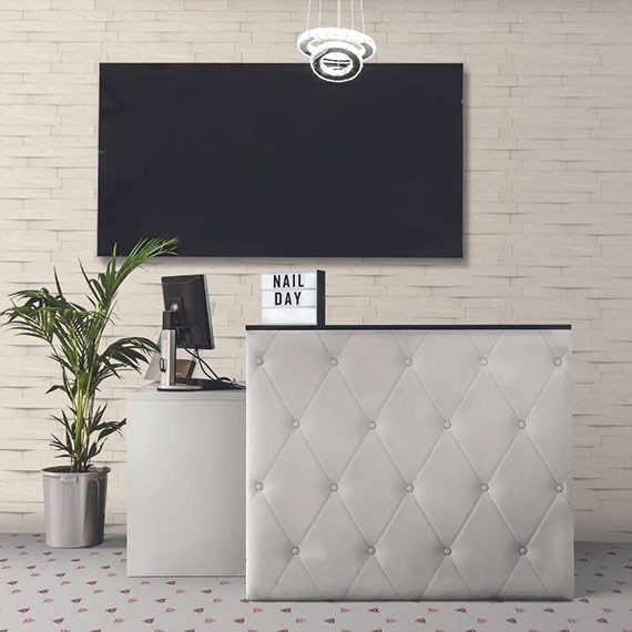 Nail salon with wall with tile that looks like white stacked stone, white tufted leather check-in desk, white, maroon & pink hexagon floor tile.