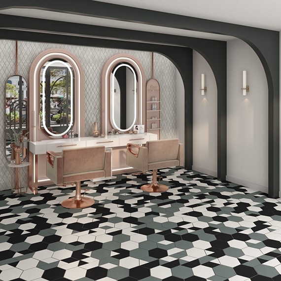 Hair salon with gray, black, and white hexagon floor tile, pink chairs, lighted mirror frames, white iridescent harlequin wall tile.