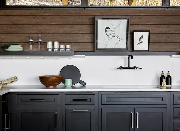 Kitchen sink with wood panels on top half of wall, white countertop and backsplash on bottom half of wall. and black cabinets.