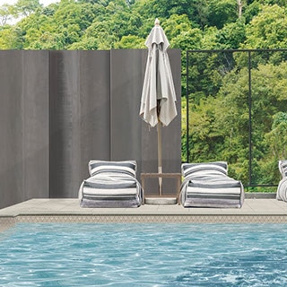 Outdoor pool with beige diamond mosaic pool tile, pool deck of beige stone look porcelain pavers, lounge chairs with white & gray striped covering.