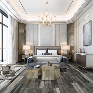 Modern bedroom design with floor tile that looks like gray seasoned wood, king bed, chaise lounge, and chandelier hanging from lighted tray ceiling.