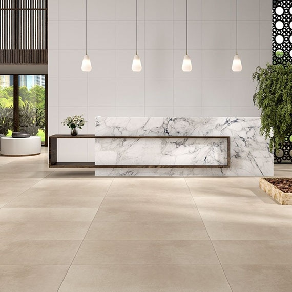 Hotel lobby with large, beige, stone-look floor tile, pendants over reception desk made of white & gray marble-look slab, and white wall tile. 