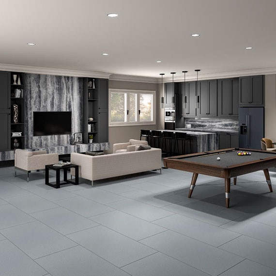 Game room with gray tile flooring, gray & white fireplace hearth and kitchenette island countertop, bar stools, black billiard table, beige sofa & chair.