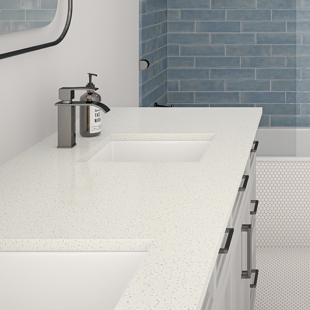 Bathroom sink with white monochromatic look countertop, shower in background with blue undulated shower tile, white mosaic on floor, and white cabinets.