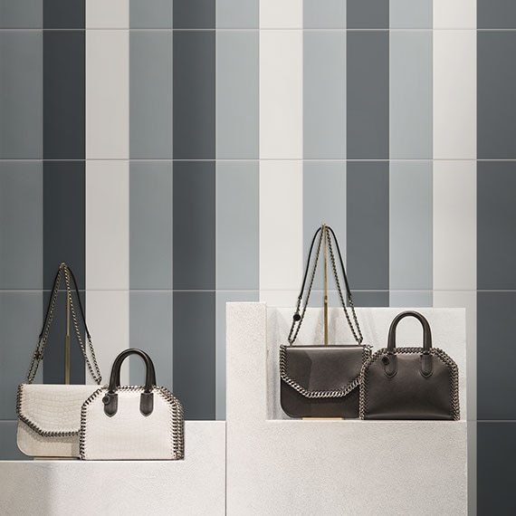 Boutique shop wall with glazed ceramic tile in vertical stripes of grey and blue. Handbags on a shelf in the foreground.