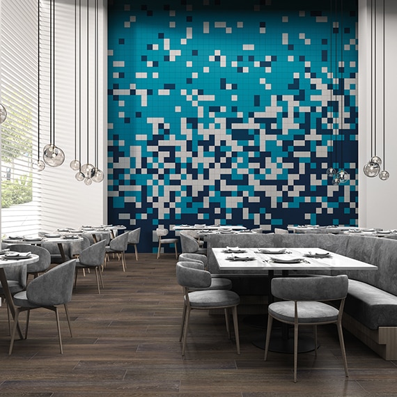 Restaurant dining room with 20-foot feature wall of navy, white, and teal tile in a random pattern, globe pendant lighting, wood look tile flooring, and tables with gray suede chairs & booths.