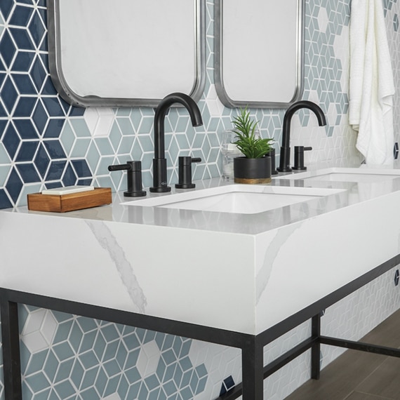 Bathroom with light blue, navy & and white cube mosaic tile backsplash and white porcelain slab countertop on vanity with black metal legs.