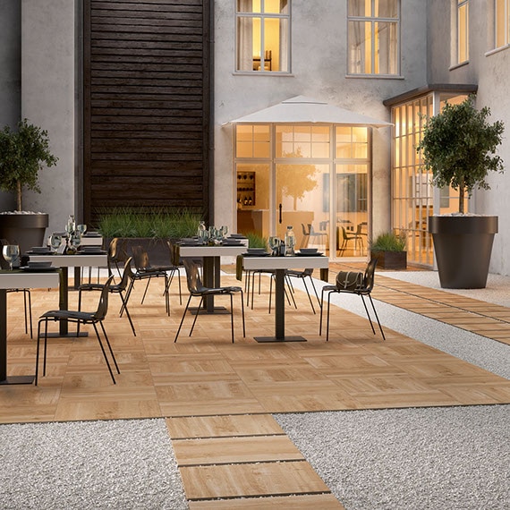 Outdoor hotel restaurant with 24” x 24” 2 centimeter porcelain pavers that look like elm wood for dining area flooring and walkway set in gravel.