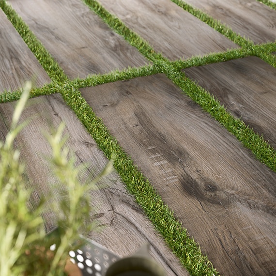 Closeup of 16" x 48" 2 centimeter porcelain pavers that look like seasoned wood, set on top of green grass.
