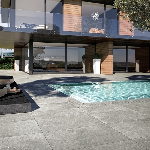 Backyard of two-story house with floor-to-ceiling windows, natural wood shiplap siding, and pool with gray stone look pavers.