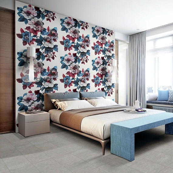 Bedroom with white slab wall tile with large white, blue, and cranberry red flowers, platform king size bed with beige & blue bedding, and blue footboard.