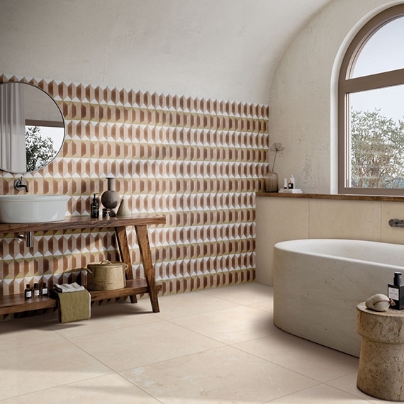 Bathroom with terracotta, peach, and white decorative wall tile, beige limestone stone look floor tile, soaker tub, vessel sink on wood vanity.
