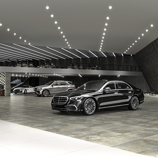 New car showroom with gray floor tile and wall tile that looks like metal tile, high ceiling with recessed lighting, mezzanine level with desks and chairs.