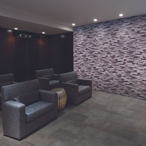 Media room with purple & lilac glass mosaic feature wall, mounted projector, projector screen, gray stone look floor tile, and 4 gray recliners.