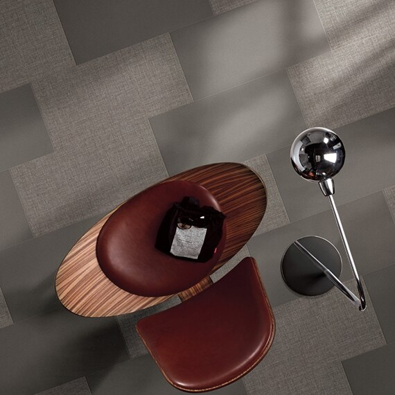 Overhead view of gray fabric look tile in random pattern with cement look tile, maroon leather & wood chair, and silver floor lamp.