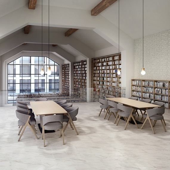 Public library with marble look tile floor, table & chairs, bookshelves, chevron wall tile, pendant lights, and beamed vaulted ceiling.
