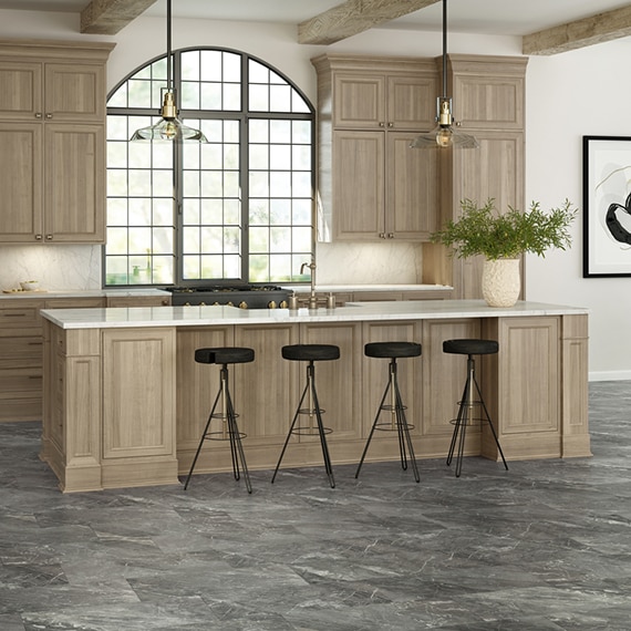 French country kitchen with gray stone look tile floor, wood cabinets, ivory/beige marble island countertop & backsplash, arched picture window.