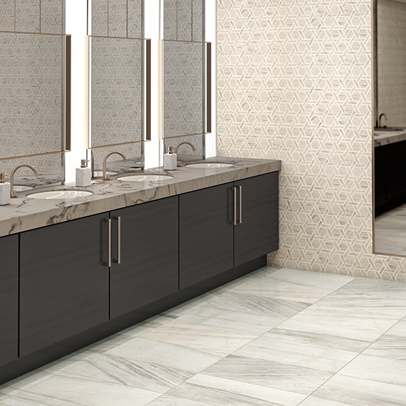 Elegant hotel public bathroom with white & gray marble floor tile, beige & gray marble hexagon wall tile, gray & beige quartzite vanity countertop, and dark wood cabinets.