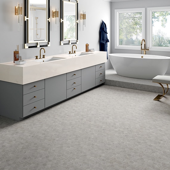 Bathroom with gray hexagon marble mosaic floor tile, free-standing bathtub in front of picture windows, and double vanity with white quartz countertop.