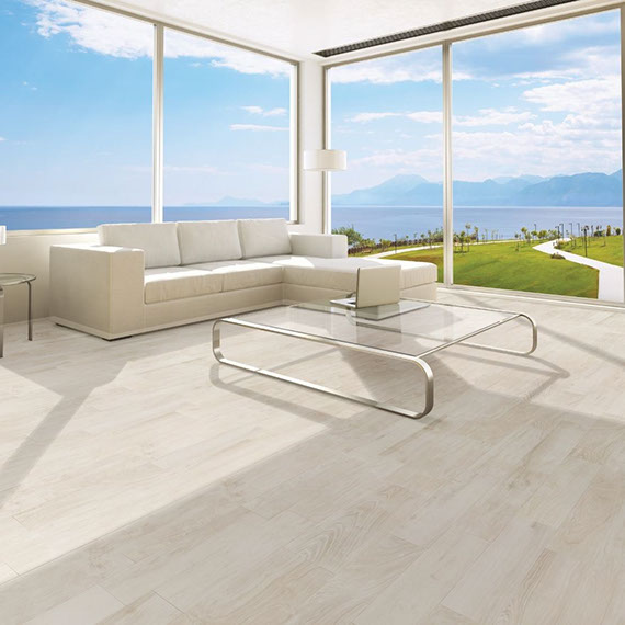 Living room with tile floor that looks like white oak flooring, off-white sofa, glass & brushed silver coffee table, and floor-to-ceiling windows with ocean scene.