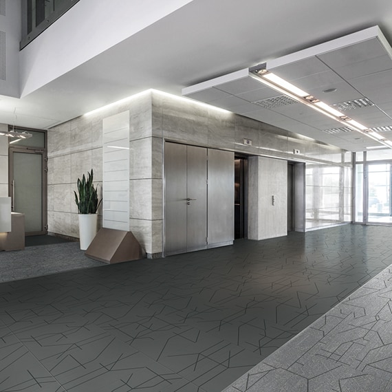 Office building elevator corridor with light and dark gray tile flooring with black design accents, light gray marble walls, and floor to ceiling windows.