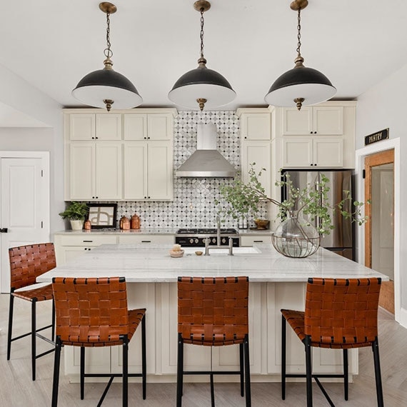 Renovated kitchen with gray natural quartzite countertops, black mirror and white & gray marble petal mosaic backsplash, white cabinets, and leather weave bar stools.
